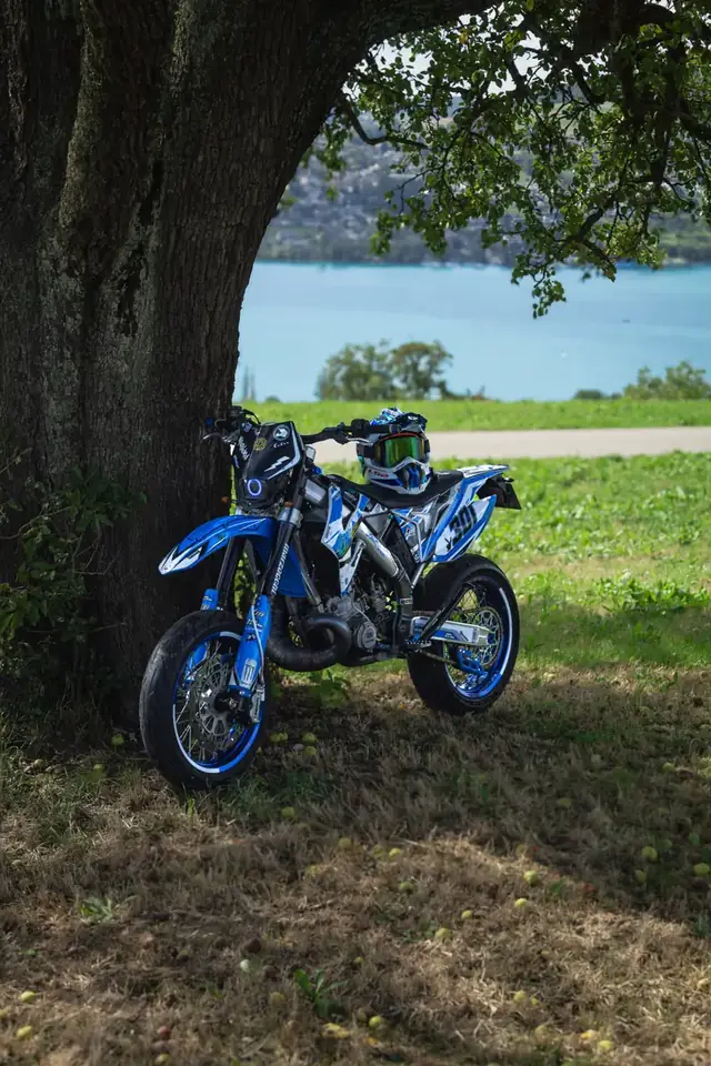 Blaue Supermoto unter einem Baum am See